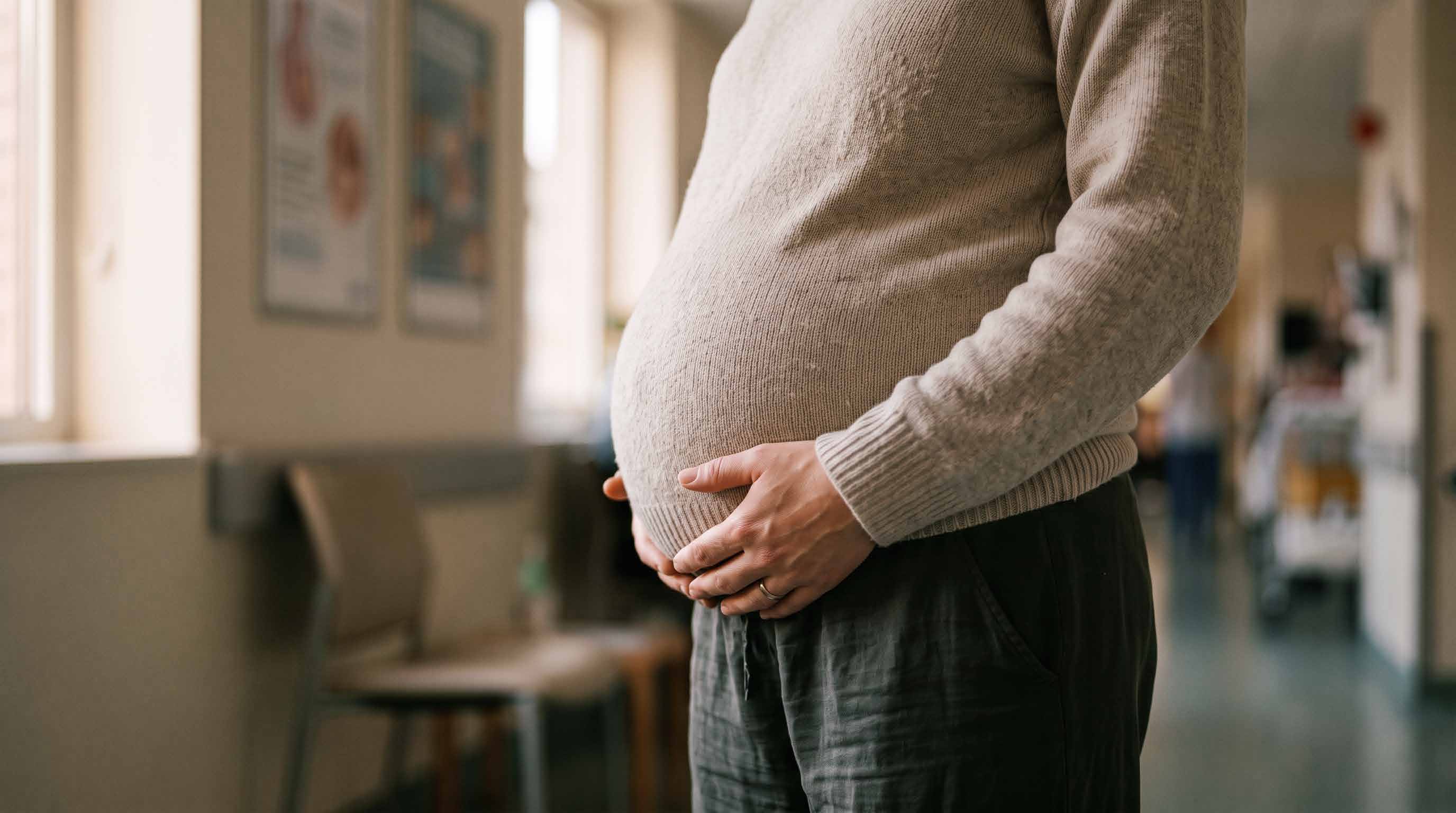 Mujer embarazada con las manos sobre el vientre, en un pasillo de un centro de salud.